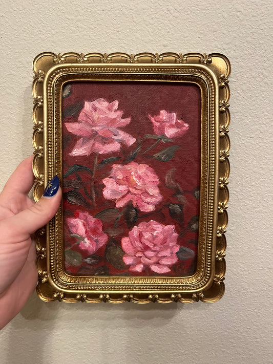Decorative painting of pink flowers against a dark red background in a gold frame held by a han