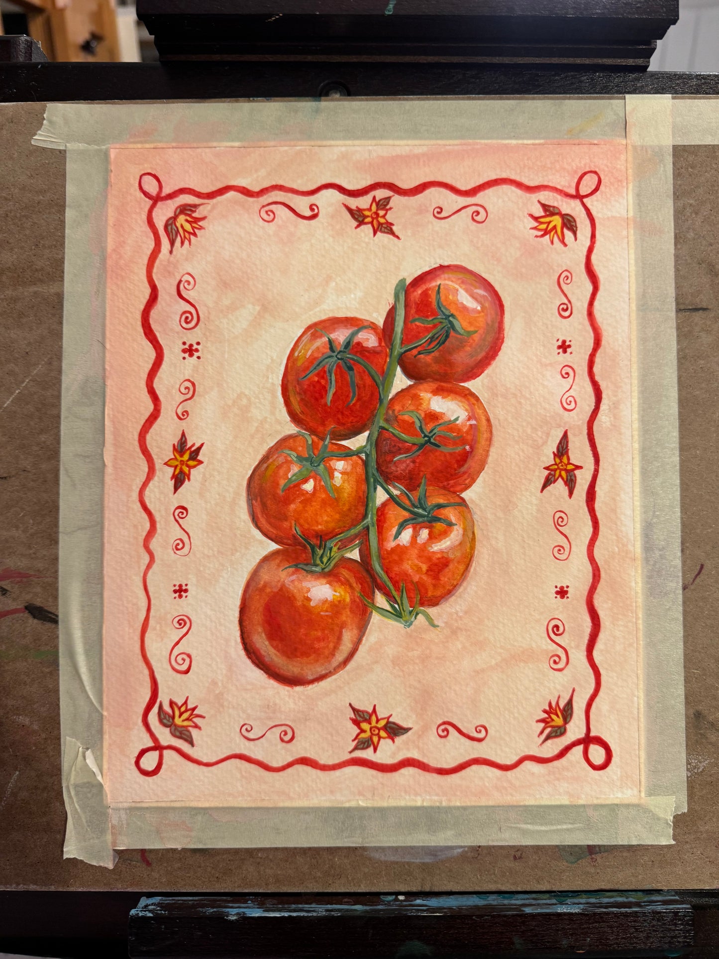 watercolor painting of tomatoes with a decorative border and pink background taped against an easel