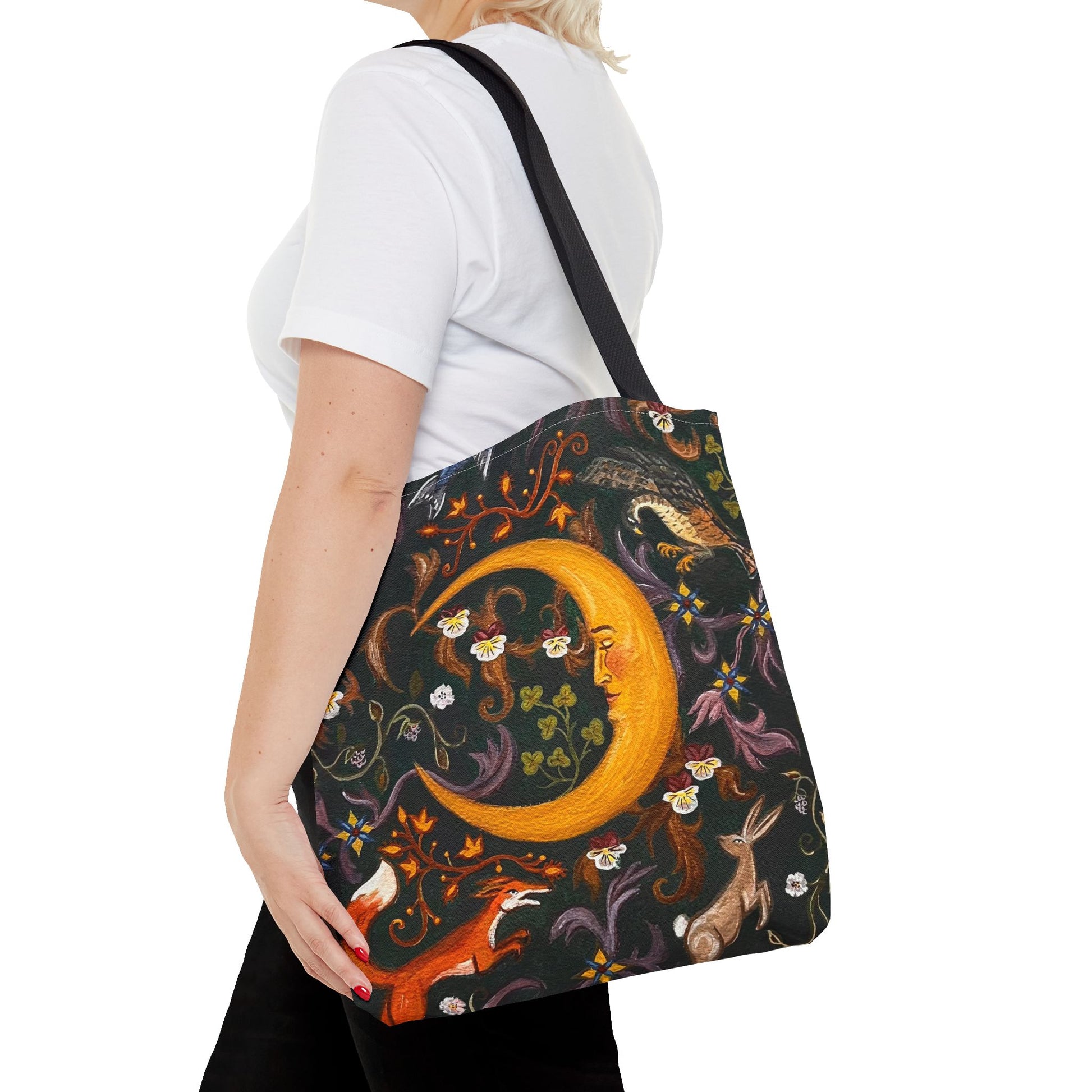 Person holding a tote bag with a fantasy design featuring a crescent moon and animals on a white background