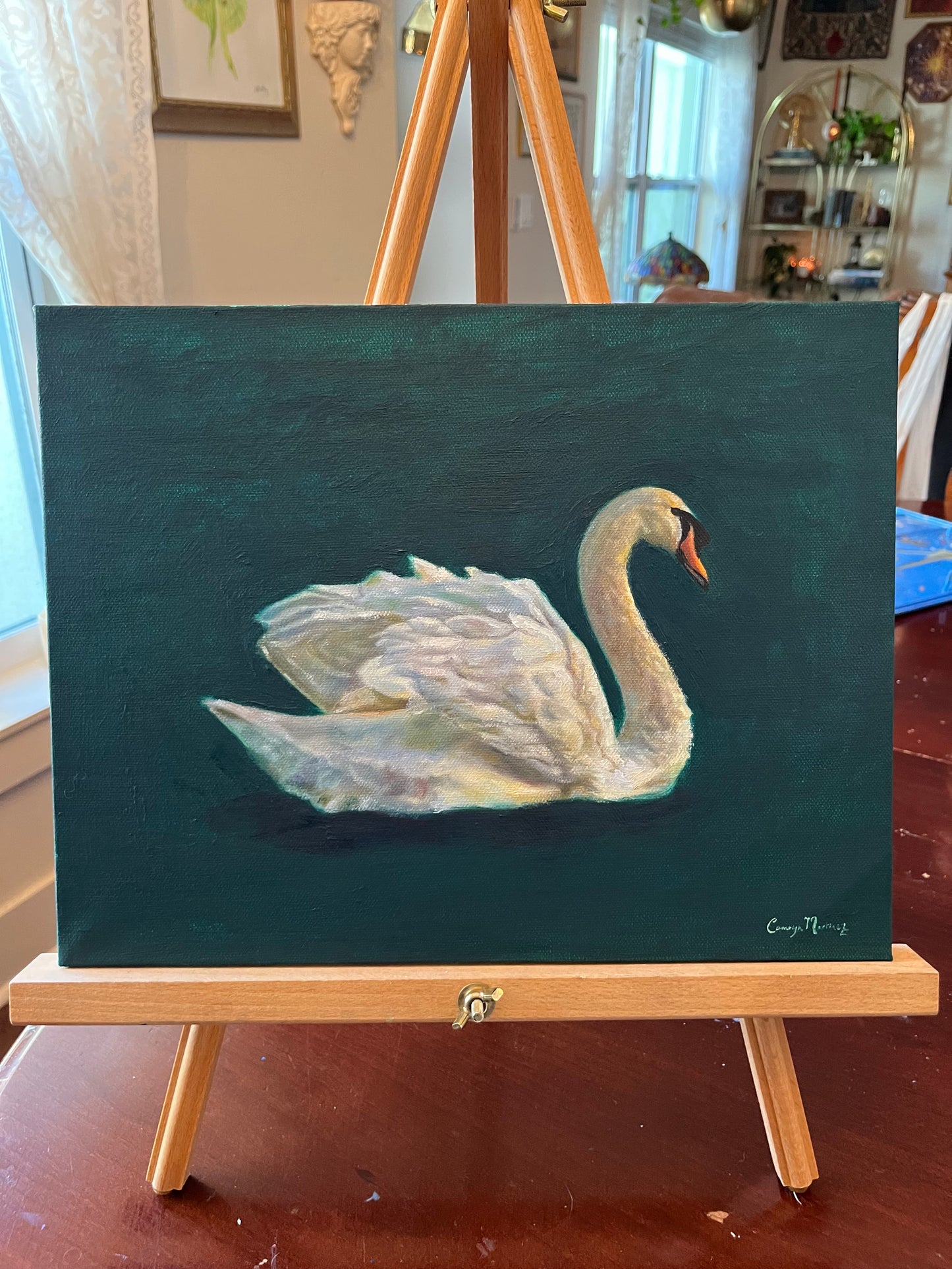 Painting of a swan on a dark green background, displayed on an easel.