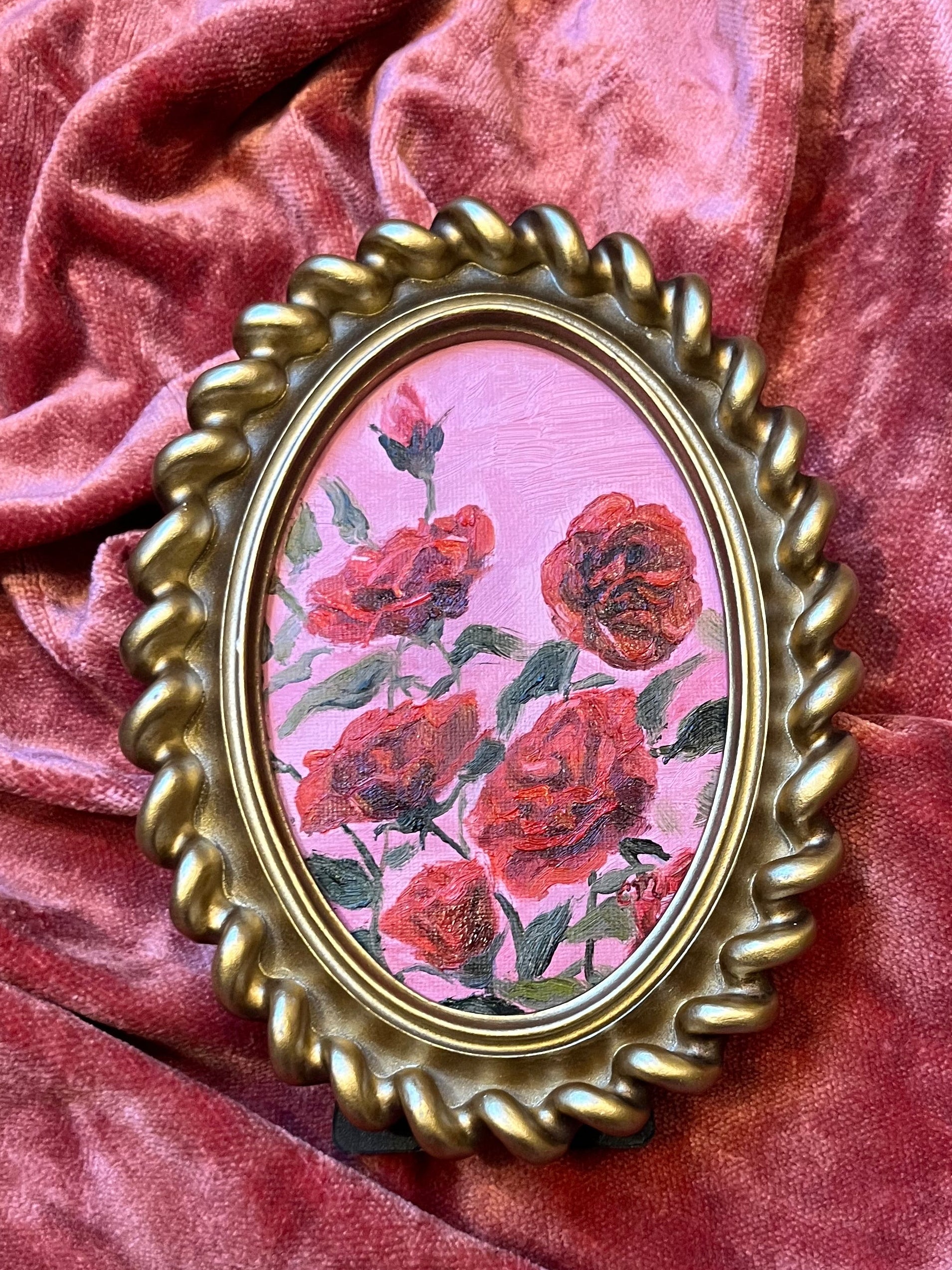 Gold-framed painting with red floral design on a pink background with a pink velvet back drop