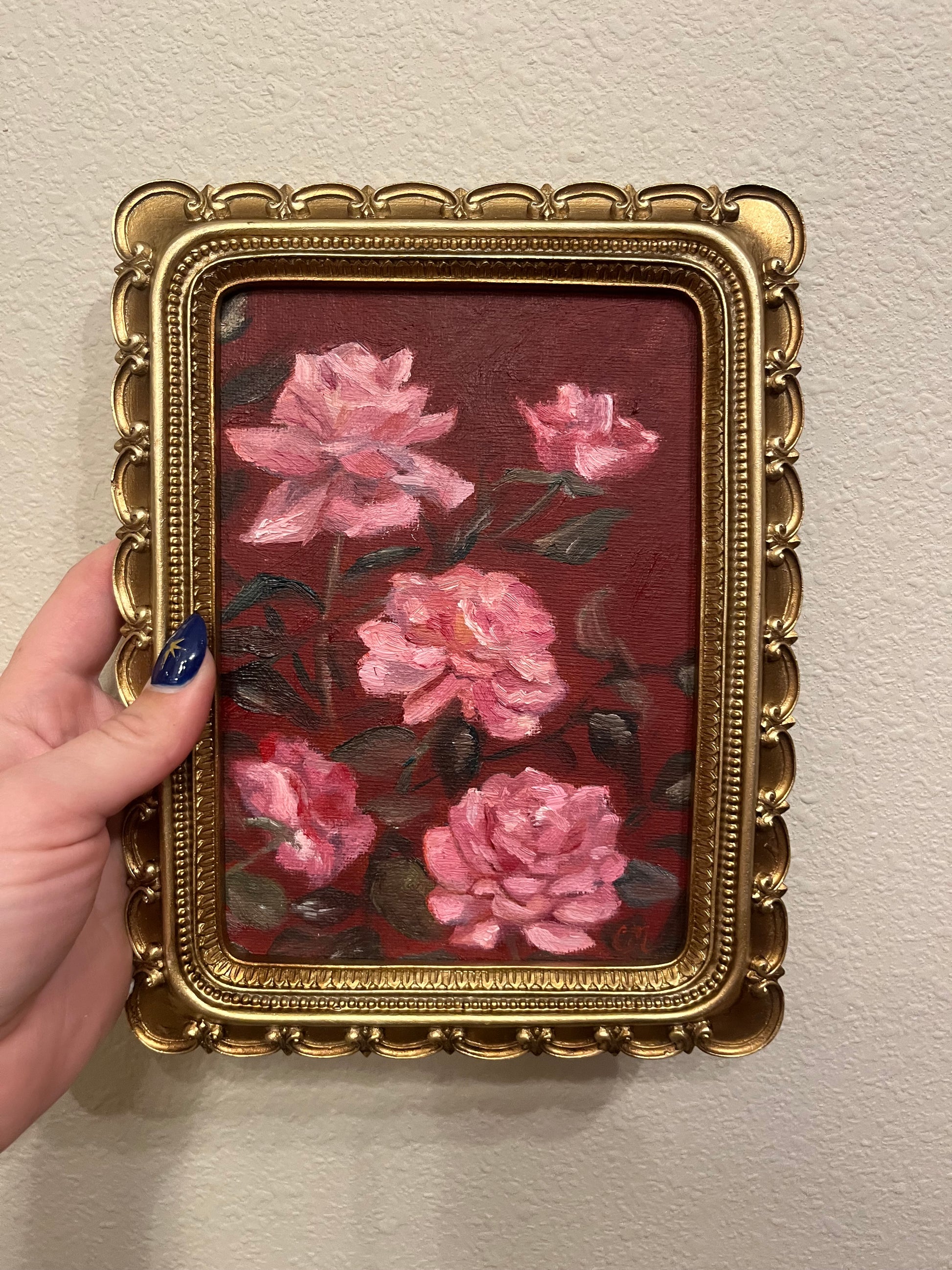 Decorative painting of pink flowers  against a dark red background in a gold frame held by a han